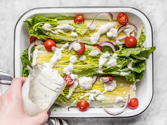 Homemade ranch dressing being poured onto a romaine salad with tomatoes and red onion
