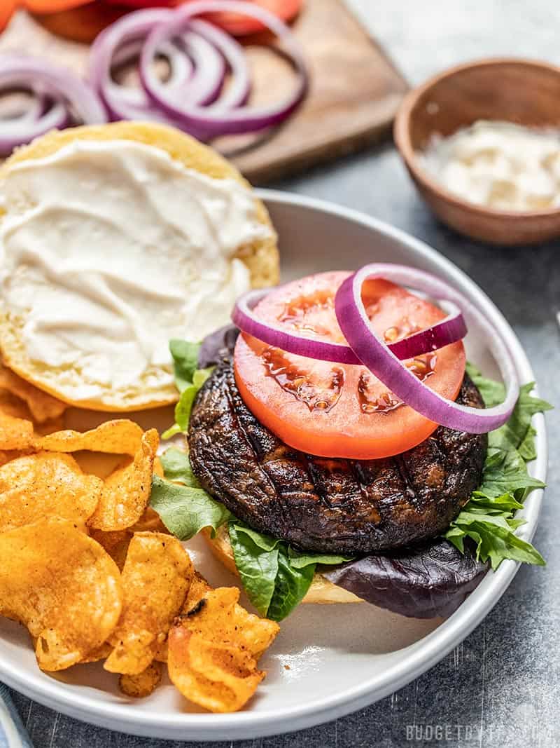 Marinated Portobello Mushroom Burger topped with tomato and onion on a plate with chips.