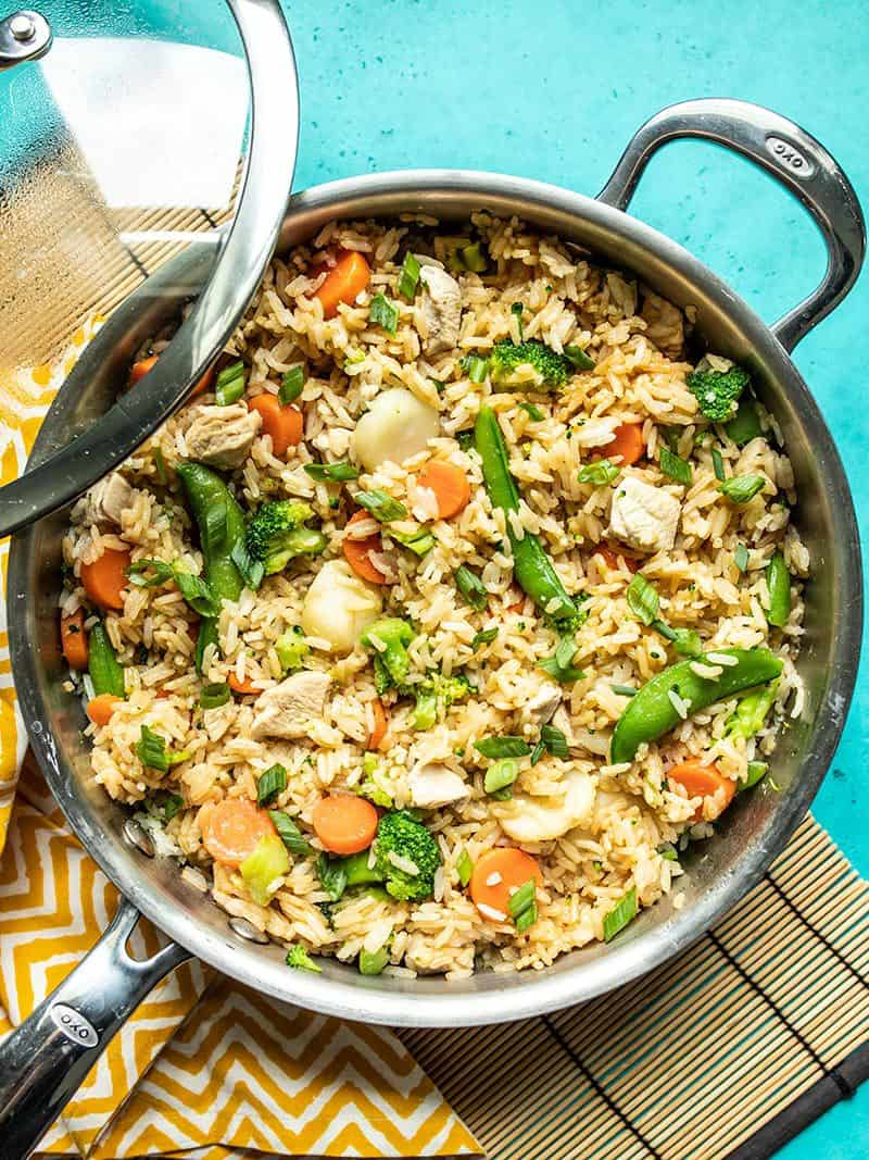 Finished skillet full of One Pot Teriyaki Chicken and rice garnished with green onion, the skillet lid resting on the side.