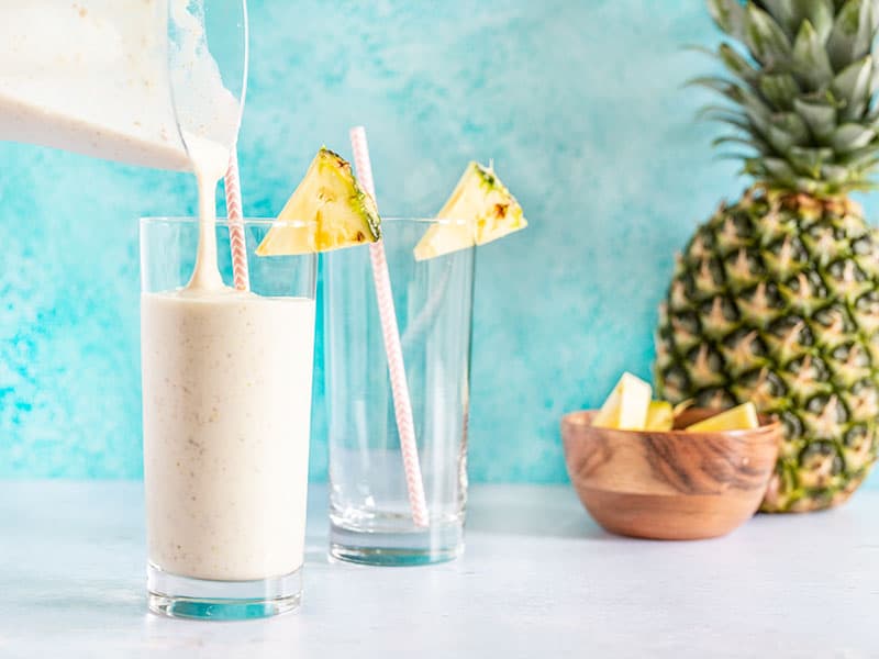 Pineapple Protein Smoothie being poured into a glass, a pineapple in the background.