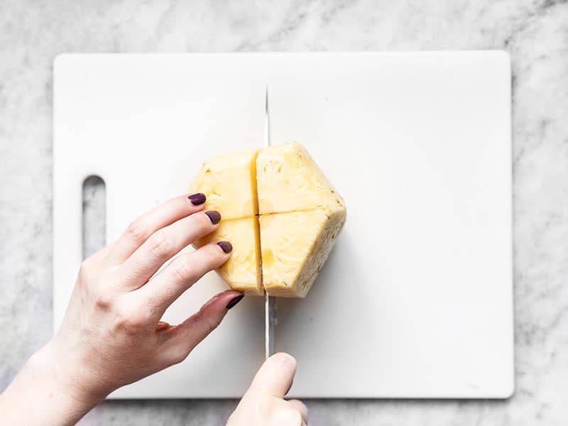 Peeled pineapple being cut into quarters.