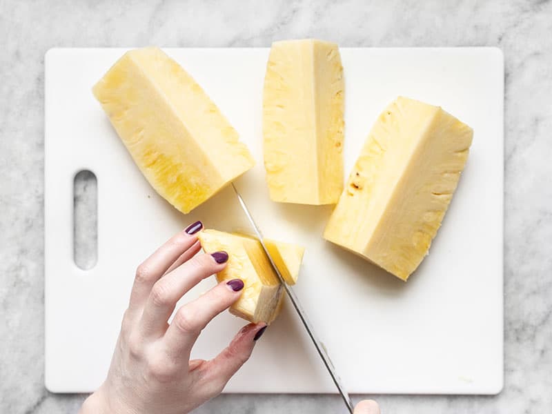 The tough core of the pineapple being sliced off a quarter..