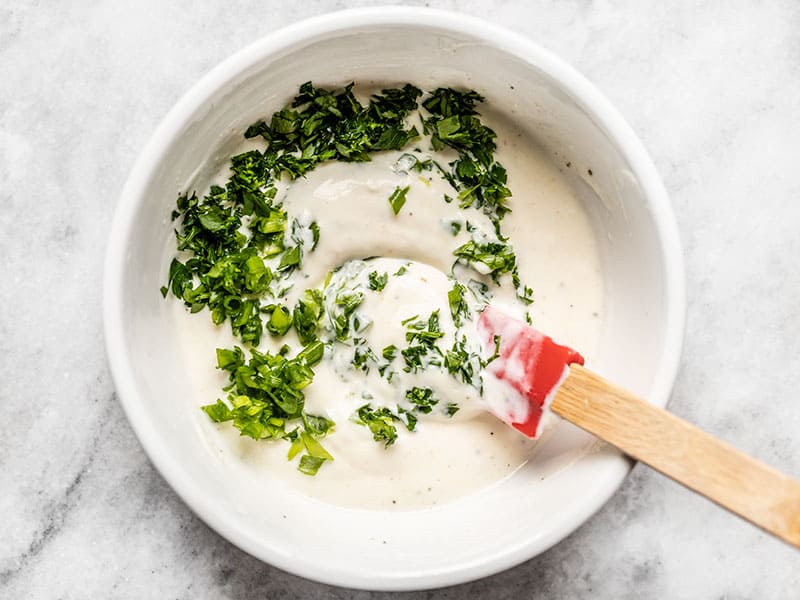 Chopped parsley and green onion being stirred into ranch dressing