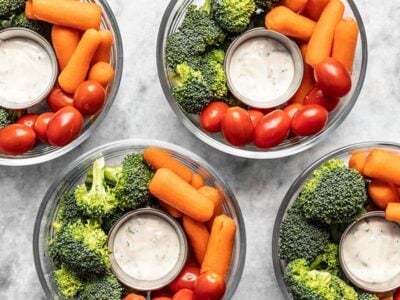 Four glass bowl veggie snack packs with ranch dressing, broccoli, and tomatoes.