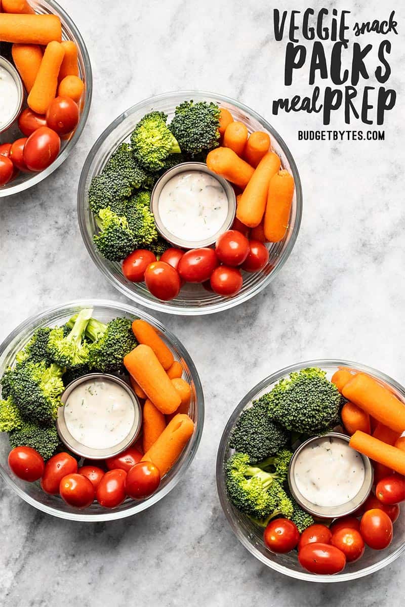 Four glass bowl containers of veggie snack packs with ranch, broccoli, carrots, and tomatoes