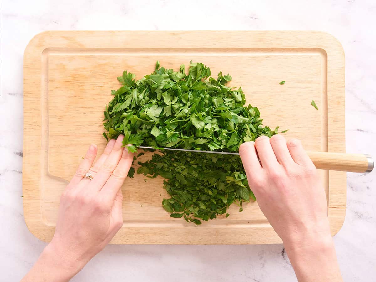 Hands using a knife to roughly chop fresh cilantro and parsley.