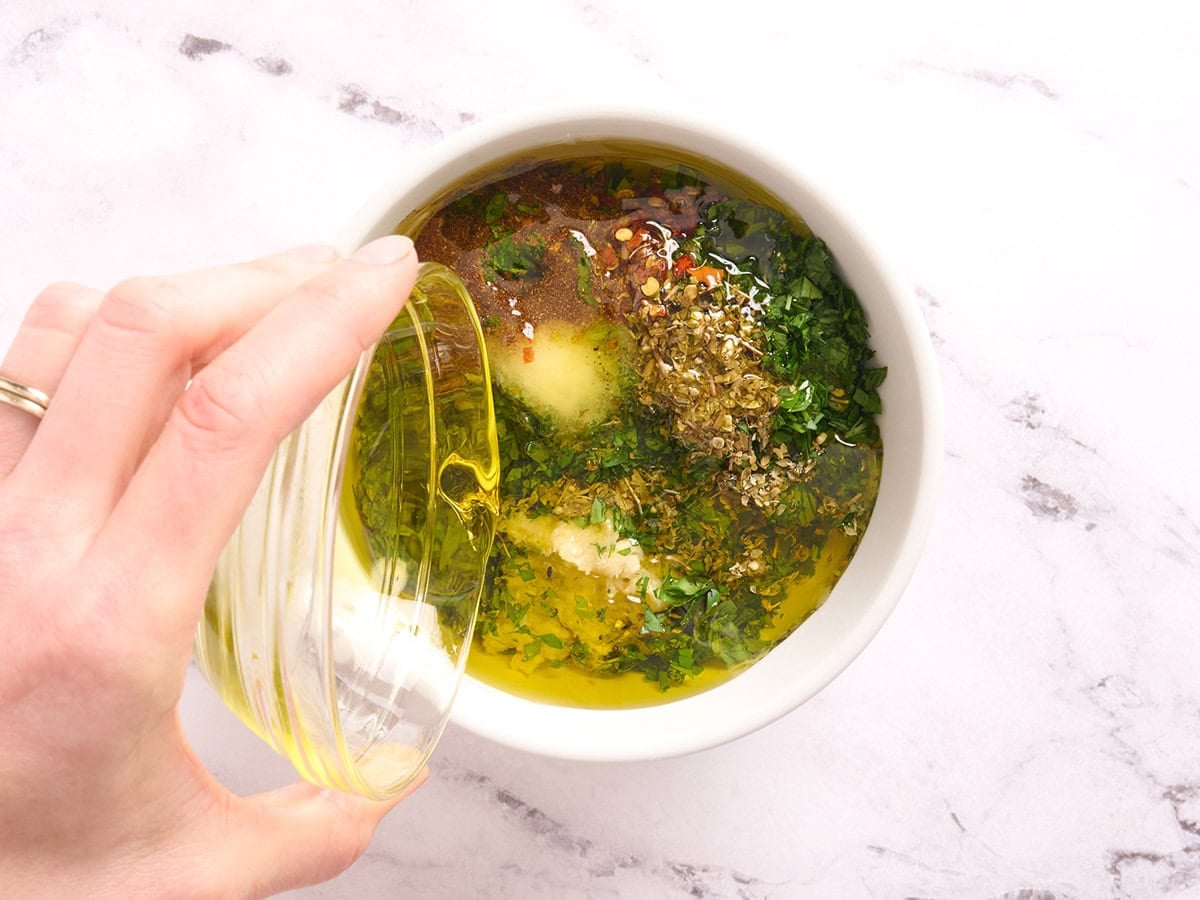 Oil being streamed into a bowl of herbs, garlic and spices.
