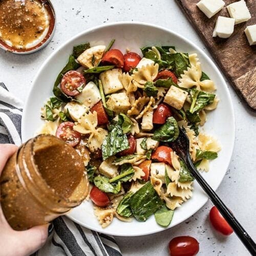 Parmesan Balsamic Vinaigrette being poured onto a bowl of Tomato Mozzarella Salad from a jar.