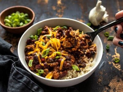Front view of a bowl of BBQ Beef and Beans topped with cheddar and green onion, and a fork lifting a bite.