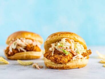 Two Baked Spicy Chicken Sandwiches against a blue wall, chips on the side.
