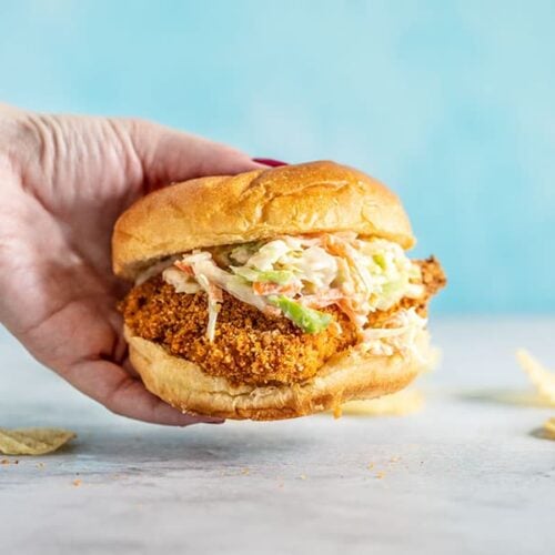 A hand holding a Baked Spicy Chicken Sandwich against a blue background.