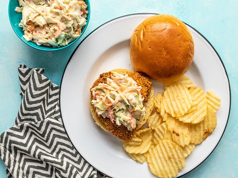One Baked Spicy Chicken Sandwich on a plate with wavy potato chips and a bowl of honey yogurt slaw on the side.