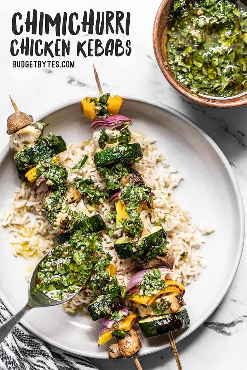 Chimichurri being drizzled onto two chimichurri chicken kebabs on a bed of rice.