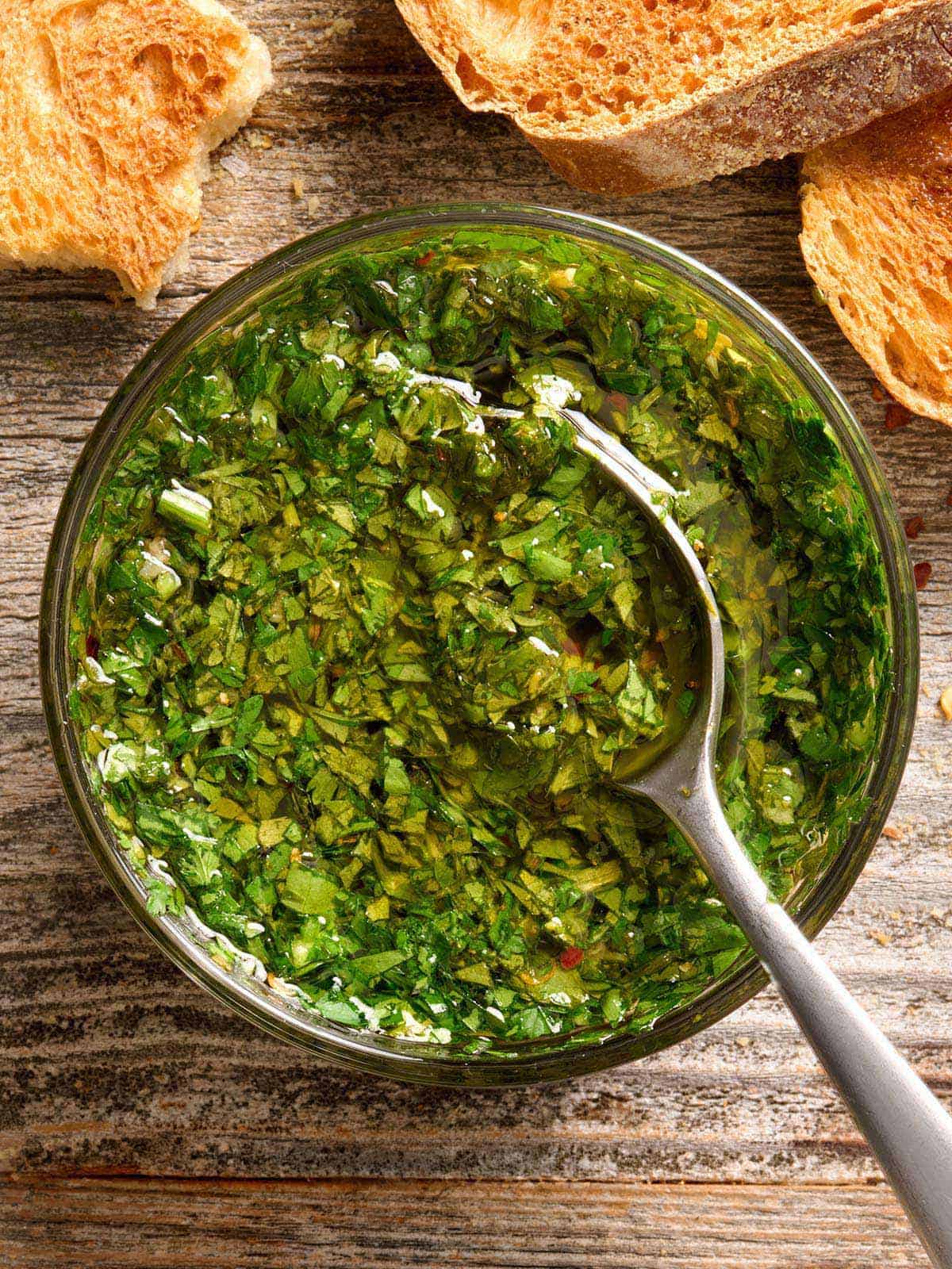 Chimichurri sauce is a tangy, fresh, and garlicky sauce that delivers big flavor to any meal. Use as a marinade, dipping sauce, or condiment. Budgetbytes.com Overhead view of a bowl of chimichurri sauce with a spoon.