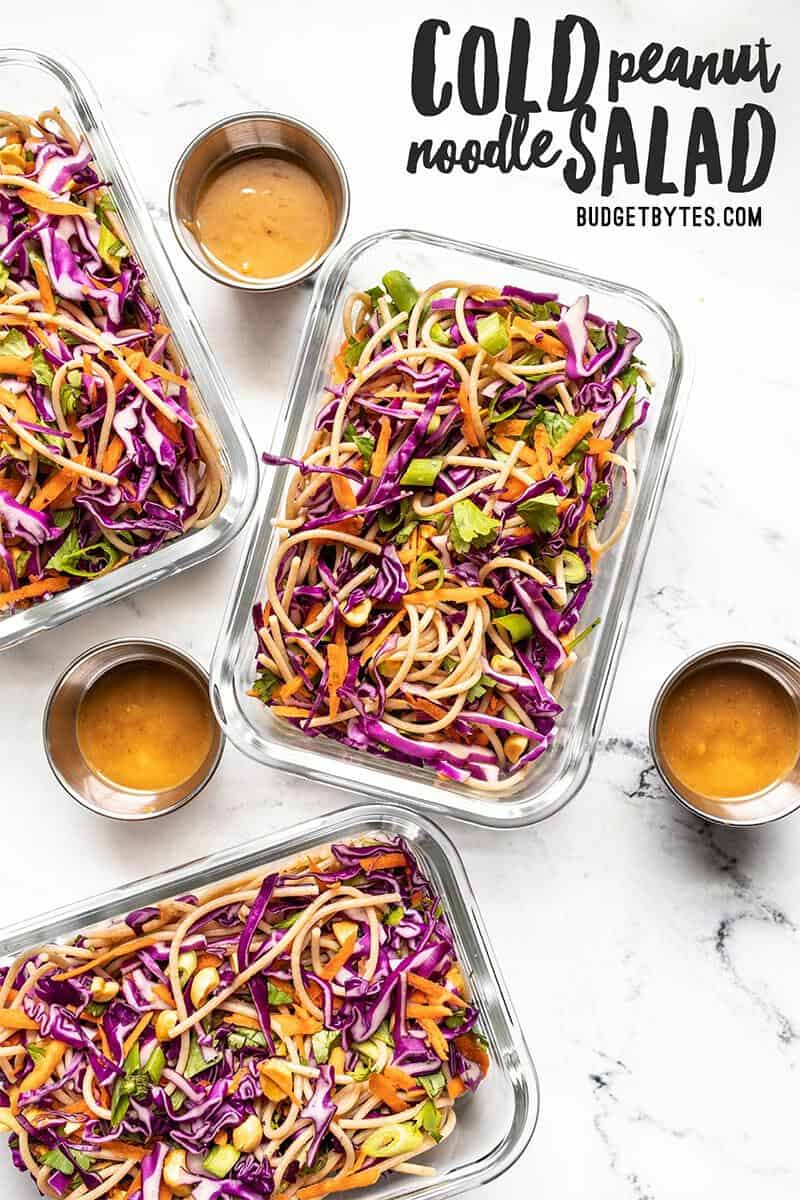 Three glass meal prep containers with cold peanut noodle salad and dressing containers on the side