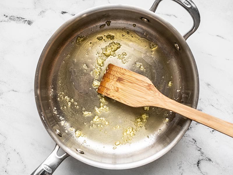 Minced garlic cooking in a skillet with oil. A wooden spatula in the skillet.