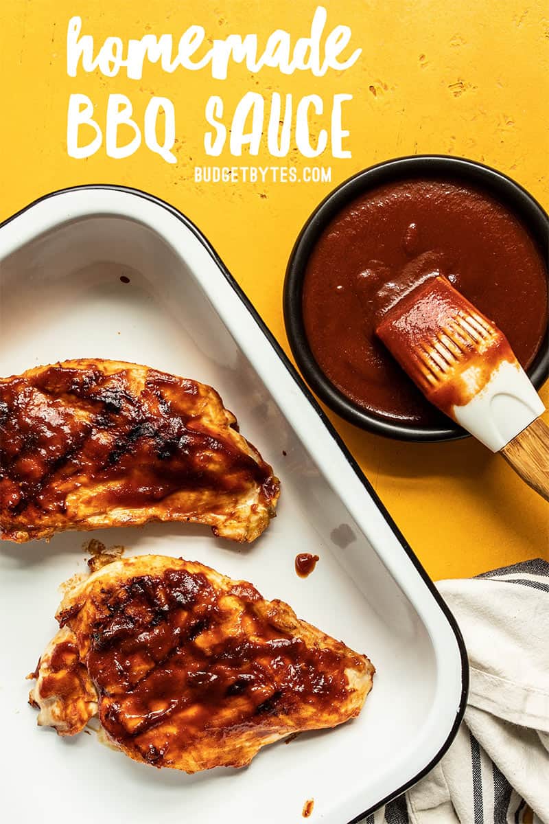 Two grilled chicken breasts with homemade bbq sauce in a white dish next to a bowl of sauce with a silicone brush