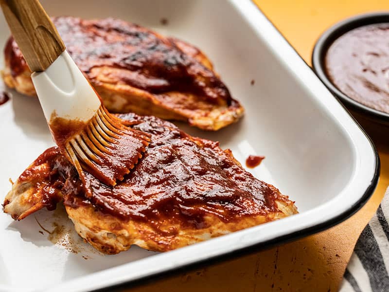 Close up of homemade BBQ sauce being brushed onto a grilled chicken breast