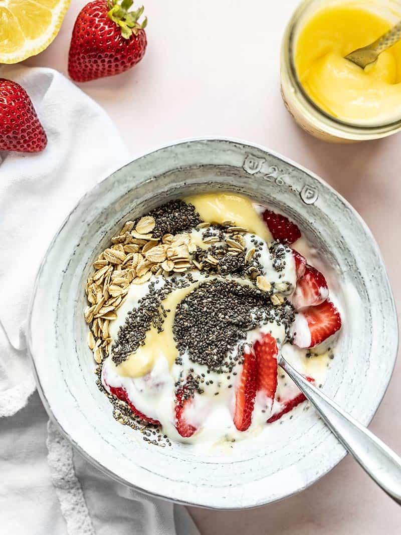Creamy yogurt and bright, citrusy lemon curd make a dreamy base for these Lemon Berry Yogurt Breakfast bowls. A few oats, chia seeds and berries make it complete. Budgetbytes.com A half-stirred lemon berry yogurt breakfast bowl with a jar of lemon curd and some strawberries on the side.