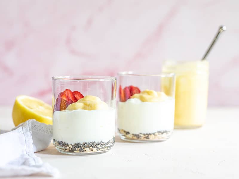 Two glasses filled with the lemon berry yogurt breakfast bowl ingredients, viewed from the side.