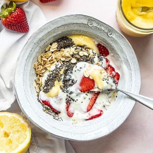 A half stirred Lemon Berry Yogurt Breakfast Bowl with a cut lemon and some strawberries near by.