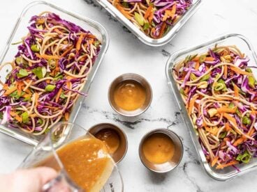 Cold Peanut Noodle Salad divided between meal prep containers, dressing being poured.