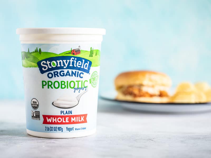 Stonyfield Organic Whole Milk Yogurt container with a baked spicy chicken sandwich in the background.