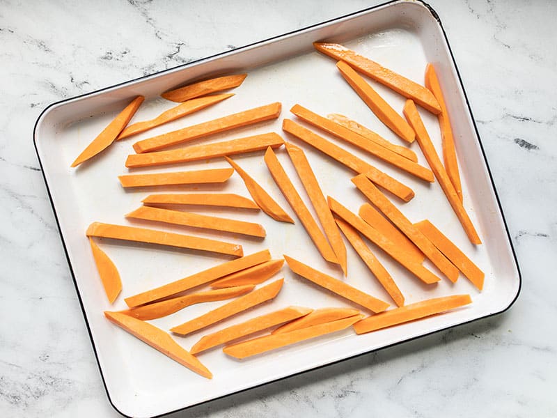 Sweet potato fries coated in oil on a baking sheet ready to bake.