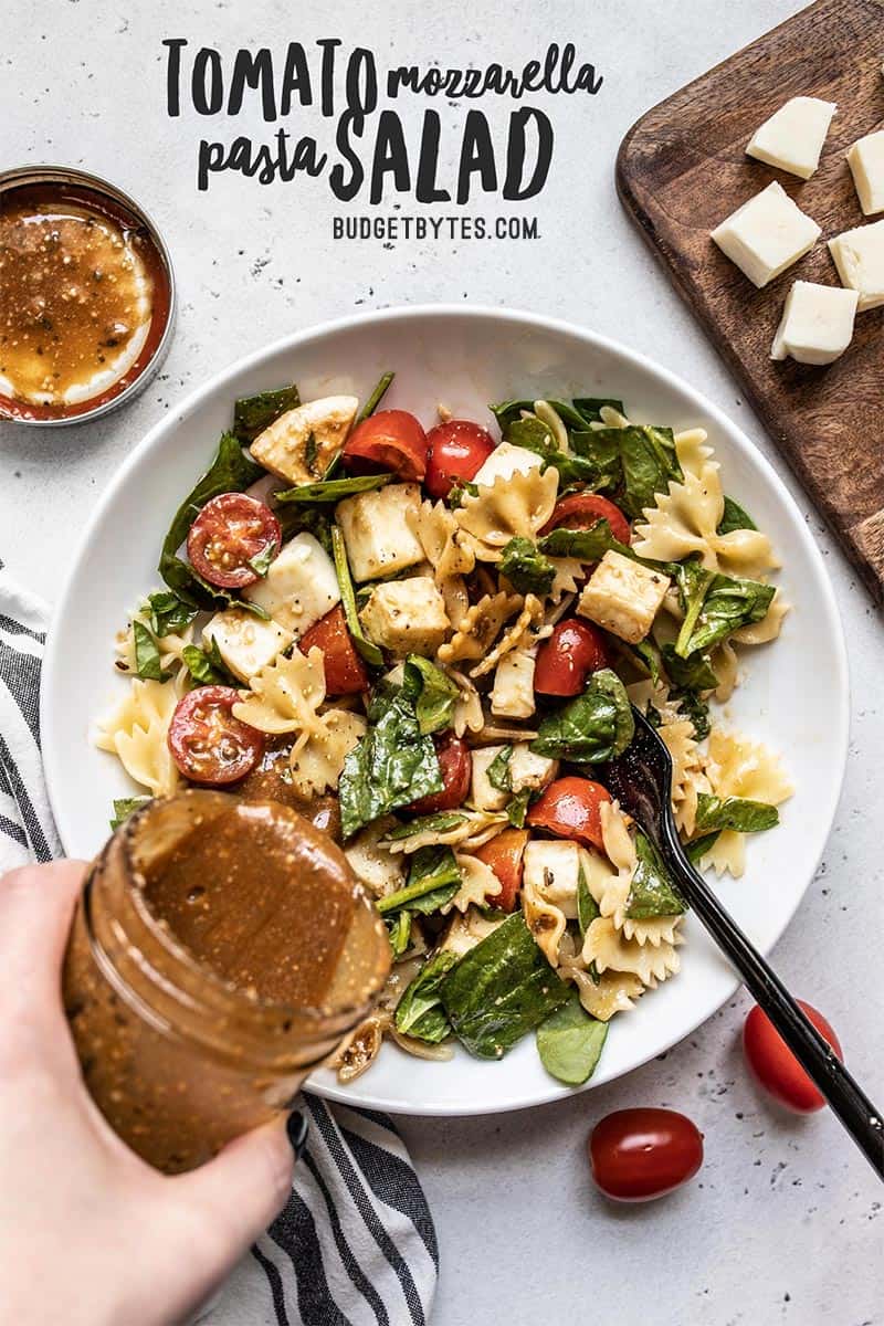 Balsamic Vinaigrette being poured from a jar over a bowl of Tomato Mozzarella Pasta Salad