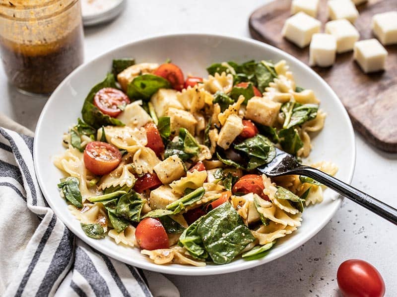 Front view of a bowl of Tomato Mozzarella Salad with a jar of dressing in the back and cubed mozzarella on the side. 