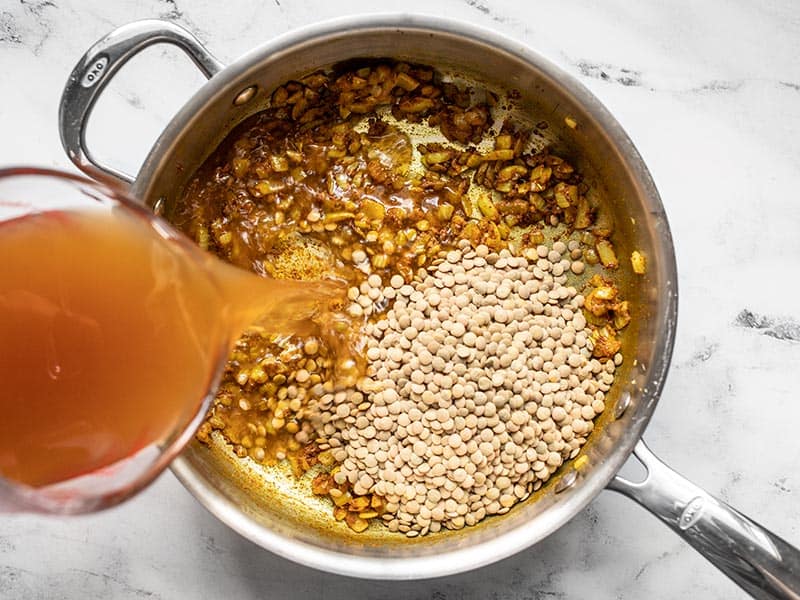 Vegetable broth being poured into the skillet