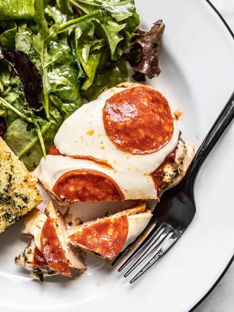 Close up of Baked Pizza Chicken on a plate with salad and garlic bread, the chicken cut into pieces.