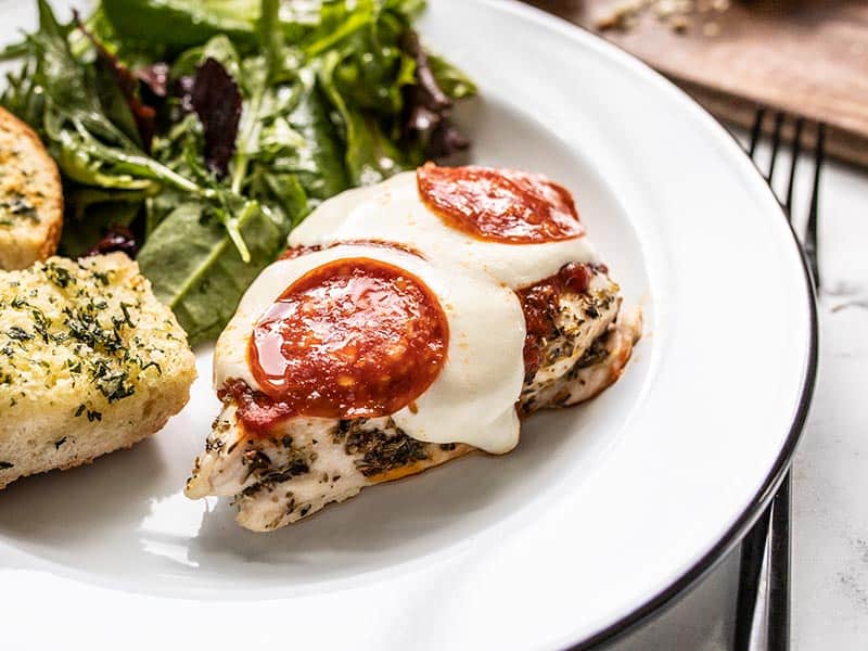 Front view of a piece of Baked Pizza Chicken on a plate with salad and garlic bread.