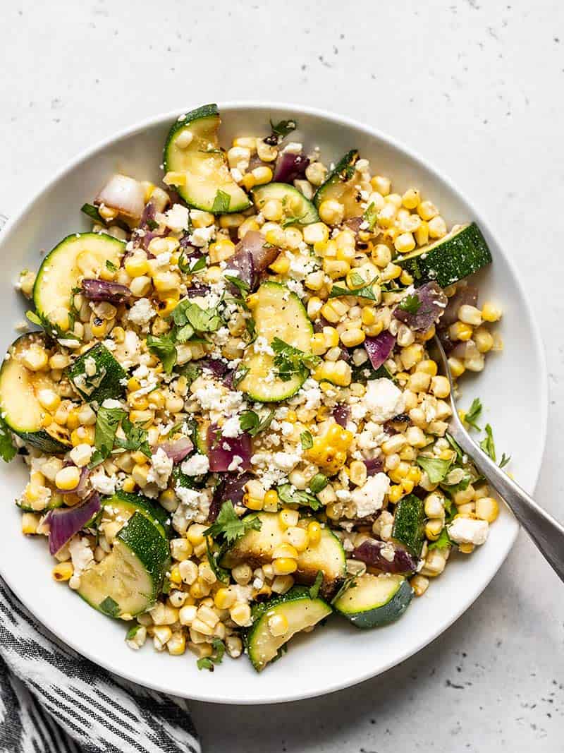 Overhead view of a large white bowl full of Charred Corn and Zucchini Salad.