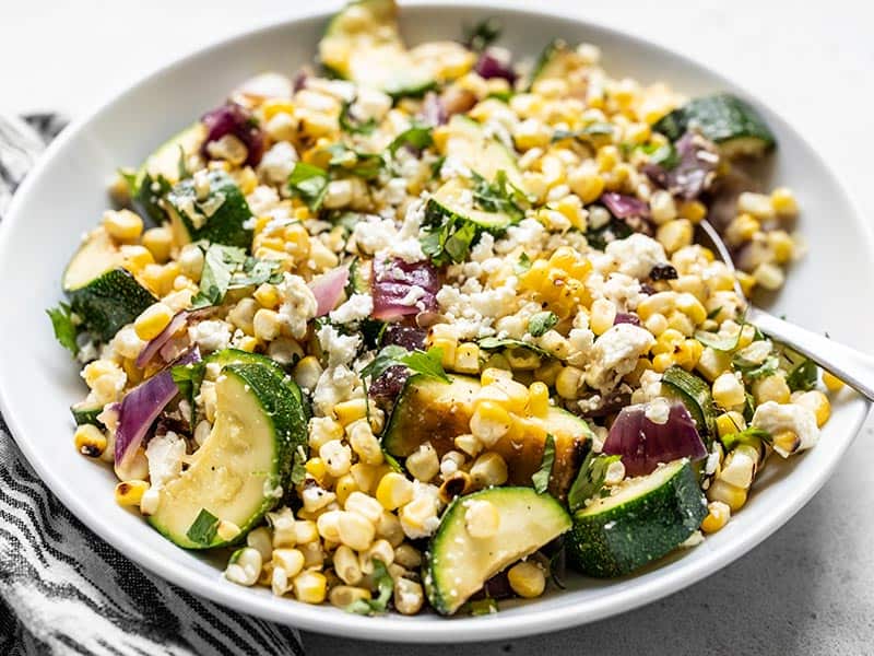Front view of a large bowl full of Charred Corn and Zucchini Salad topped with crumbled feta and cilantro