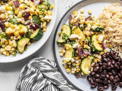 A plate filled with Charred Corn and Zucchini Salad, black beans, and rice, next to a bowl of the corn and zucchini salad.