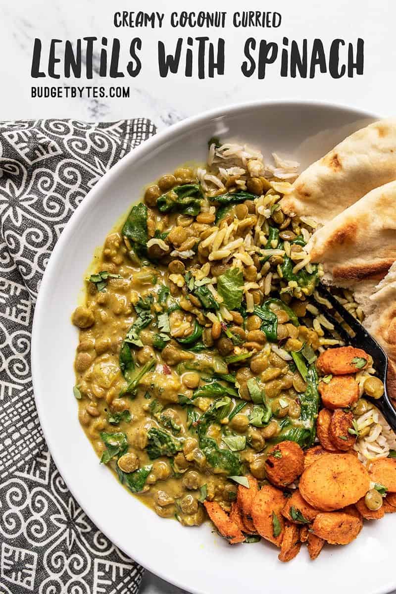 Overhead view of a plate of Creamy Coconut Curry Lentils with Spinach along side roasted carrots, rice, and naan