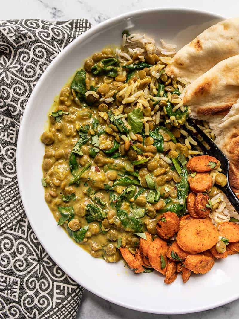 Close up overhead view of Creamy Coconut Curry Lentils with Spinach on a plate with curry roasted carrots, rice, and naan.