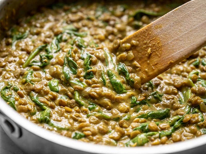Close up of Creamy Coconut Curry Lentils and Spinach being stirred in the skillet