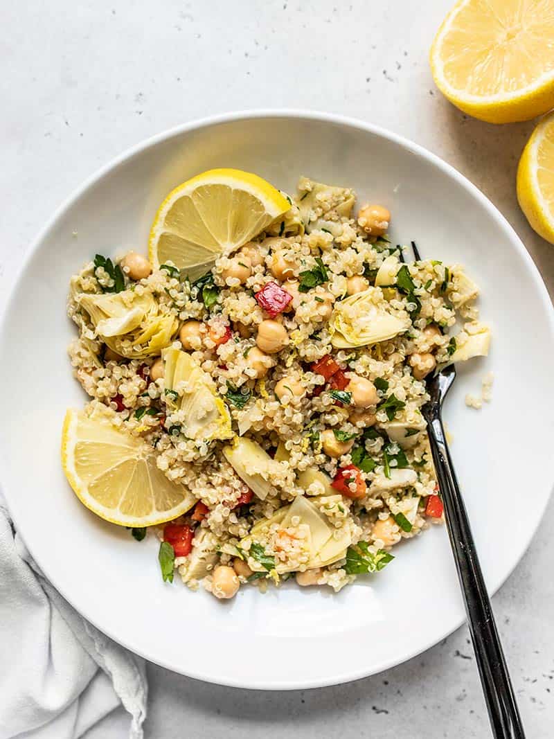 Overhead view of a bowl of Lemony Artichoke and Quinoa Salad with lemon wedges and a black fork.