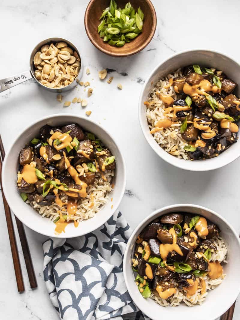 Overhead view of three bowls of Soy Glazed Eggplant served with rice, peanuts, and green onion