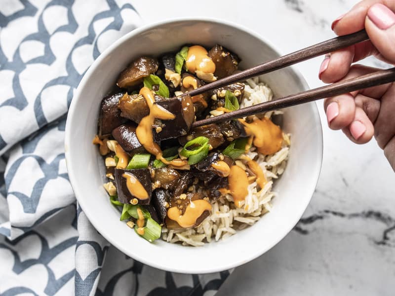 A piece of Soy Glazed Eggplant being picked up out of the bowl with chopsticks.