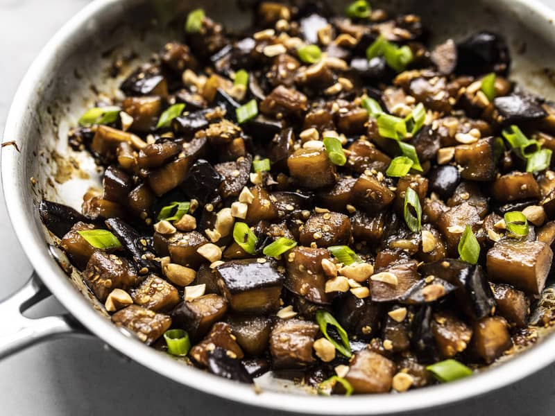 Close up side view of Soy Glazed Eggplant in the skillet, topped with peanuts and green onion