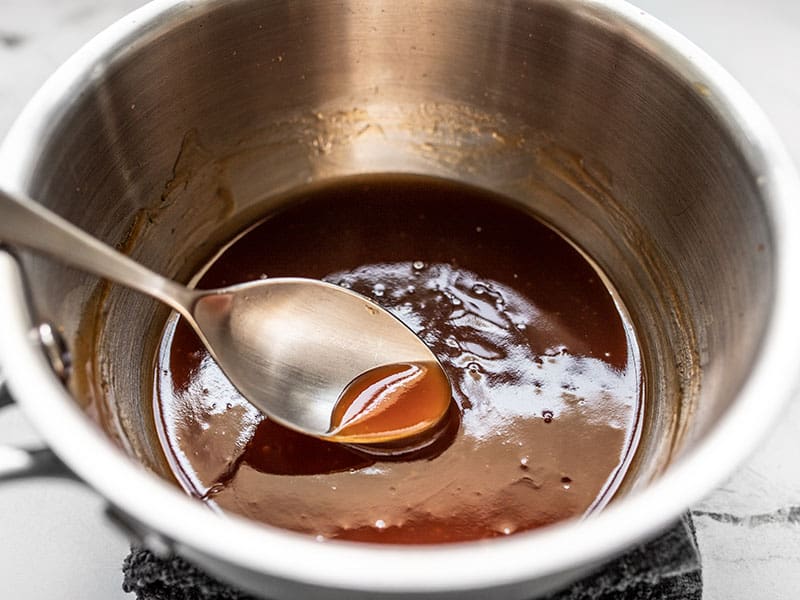 Shiny cooked sweet and sour sauce in the pot, being scooped with a spoon.