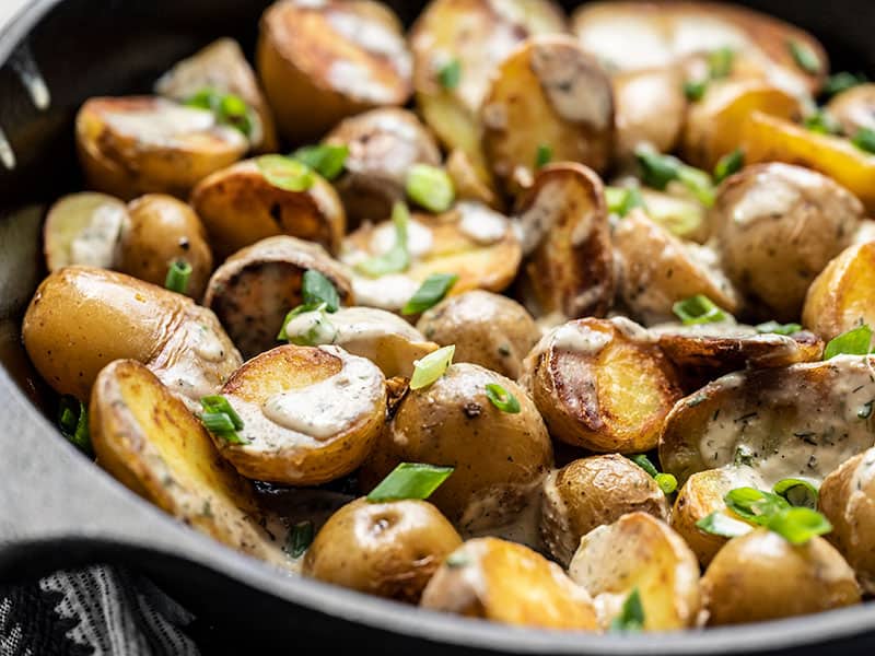 These Crispy Potatoes with Lemon Dill Tahini Dressing are like a deconstructed vegan potato salad, with a creamy homemade dressing. BudgetBytes.com Close side view of a skillet full of potatoes topped with tahini dressing and green onion