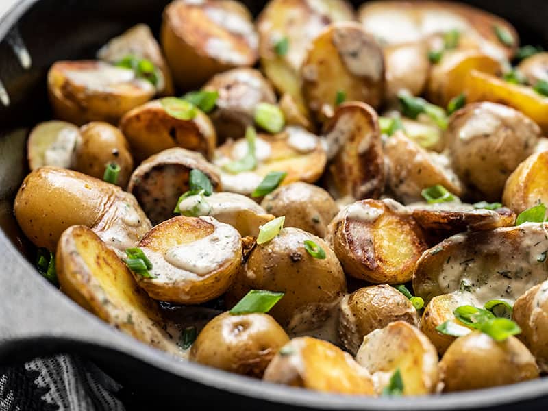 Close side view of a skillet full of potatoes topped with tahini dressing and green onion