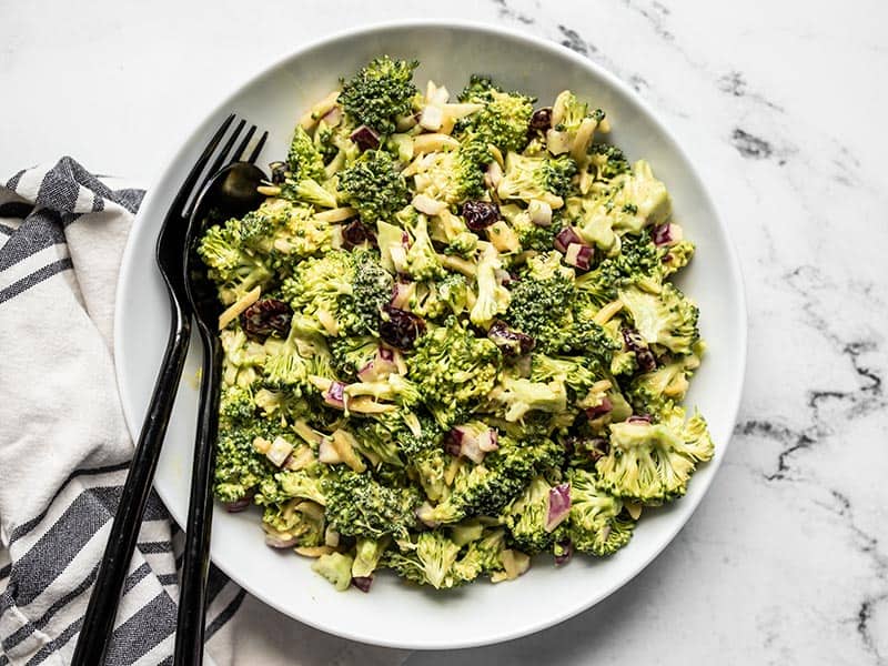 Finished honey mustard broccoli salad in a bowl, seen from above, with black fork and spoon in the side of the bowl.