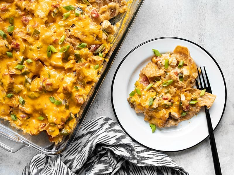 This made from scratch King Ranch Chicken Casserole has layers of chicken, tortillas, cheese, and a creamy sauce, with NO canned soups! BudgetBytes.com The casserole dish next to a plate with a serving of King Ranch Chicken Casserole