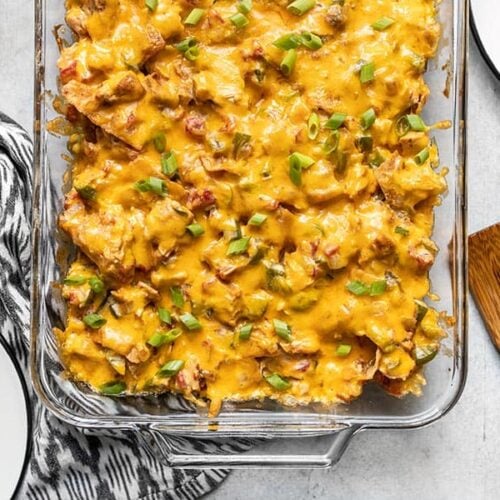 Overhead view of the bottom half of the casserole dish with baked King Ranch Chicken Casserole and two empty plates on the sides