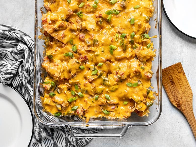 This made from scratch King Ranch Chicken Casserole has layers of chicken, tortillas, cheese, and a creamy sauce, with NO canned soups! BudgetBytes.com Overhead view of the bottom half of the casserole dish with baked King Ranch Chicken Casserole and two empty plates on the sides